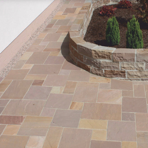 Paveworld Autumn Brown Indian Sandstone patio paving laid in mixed size pattern beside curved stone wall
