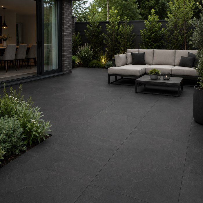 Anthracite porcelain patio with 900x600 slabs laid in a contemporary garden with outdoor seating and dark landscaped borders.