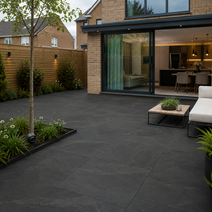 Anthracite porcelain paving laid outside a modern UK house with black-framed doors, outdoor seating and contemporary planting. 