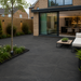 Anthracite porcelain paving laid outside a modern UK house with black-framed doors, outdoor seating and contemporary planting. 