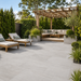 Kandla Grey porcelain patio slabs laid in a modern garden with pergola seating, sun loungers and landscaped planting.