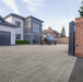 Modern house with a driveway and car, featuring a gate and surrounding landscape.