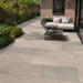 Raj Green porcelain patio with outdoor seating beside a modern brick house and landscaped garden borders.