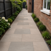 Raj Green porcelain paving laid in a side path beside a UK brick house with planting borders and black fencing.