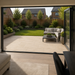 View from inside a UK home looking out onto a sand porcelain patio with garden seating, lawn and landscaped borders.
