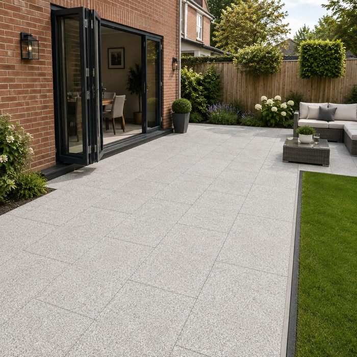 Silver Granite porcelain paving laid at the rear of a modern English brick house with bifold doors, garden furniture and lawn edge.