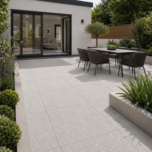 Silver Granite porcelain paving installed at a modern rendered rear extension with black aluminium doors, outdoor dining set and raised planters.