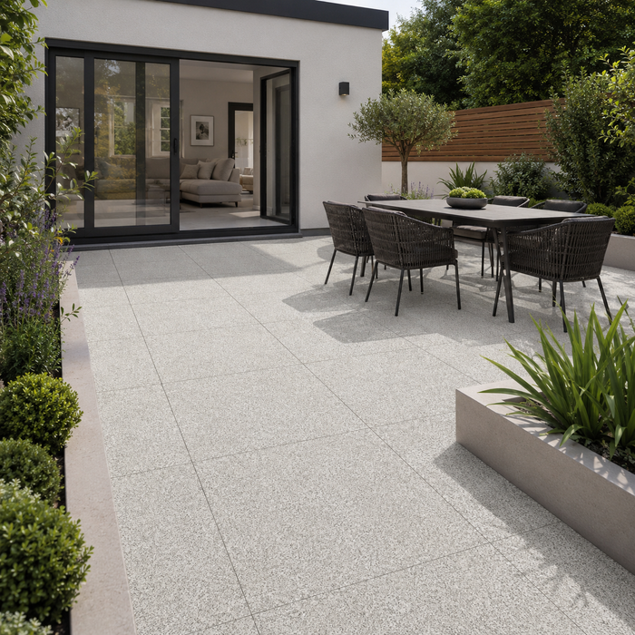 Silver Granite porcelain paving installed at a modern rendered rear extension with black aluminium doors, outdoor dining set and raised planters.
